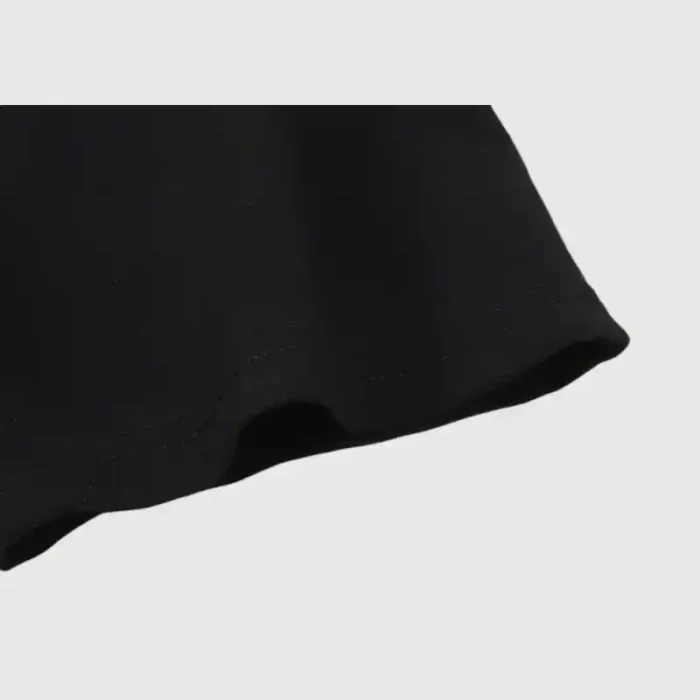 Close-up of a black fabric edge from a Hellstar Path To Paradise T-shirt against a light gray background, highlighting the texture and stitching detail of the material.